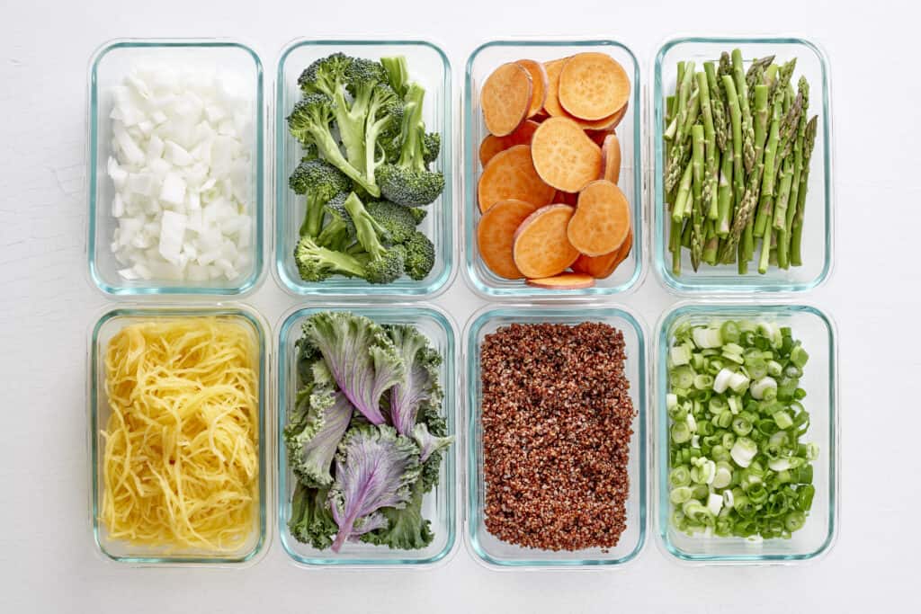 Glass meal prep containers with vegetables, quinoa, pasta, and fresh ingredients organized for healthy eating