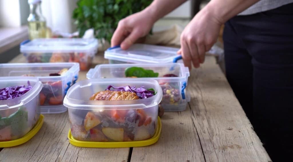 Person preparing healthy meal prep containers with grilled chicken, vegetables, and fresh ingredients