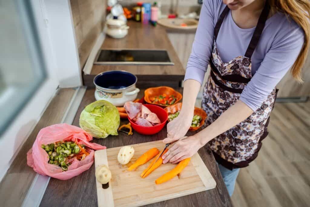 Woman slicing carrots on cutting board surrounded by colorful fresh vegetables in modern kitchen