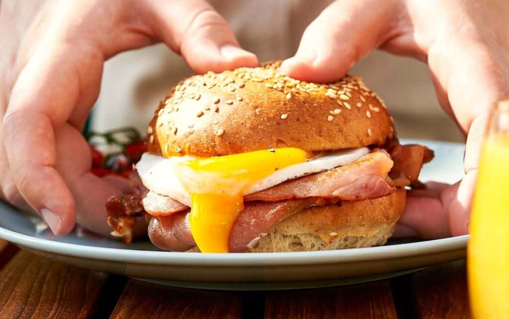 A delicious breakfast sandwich with egg, cheese, and bacon on a toasted English muffin, showcasing the dietary fat content often found in satisfying morning meals
