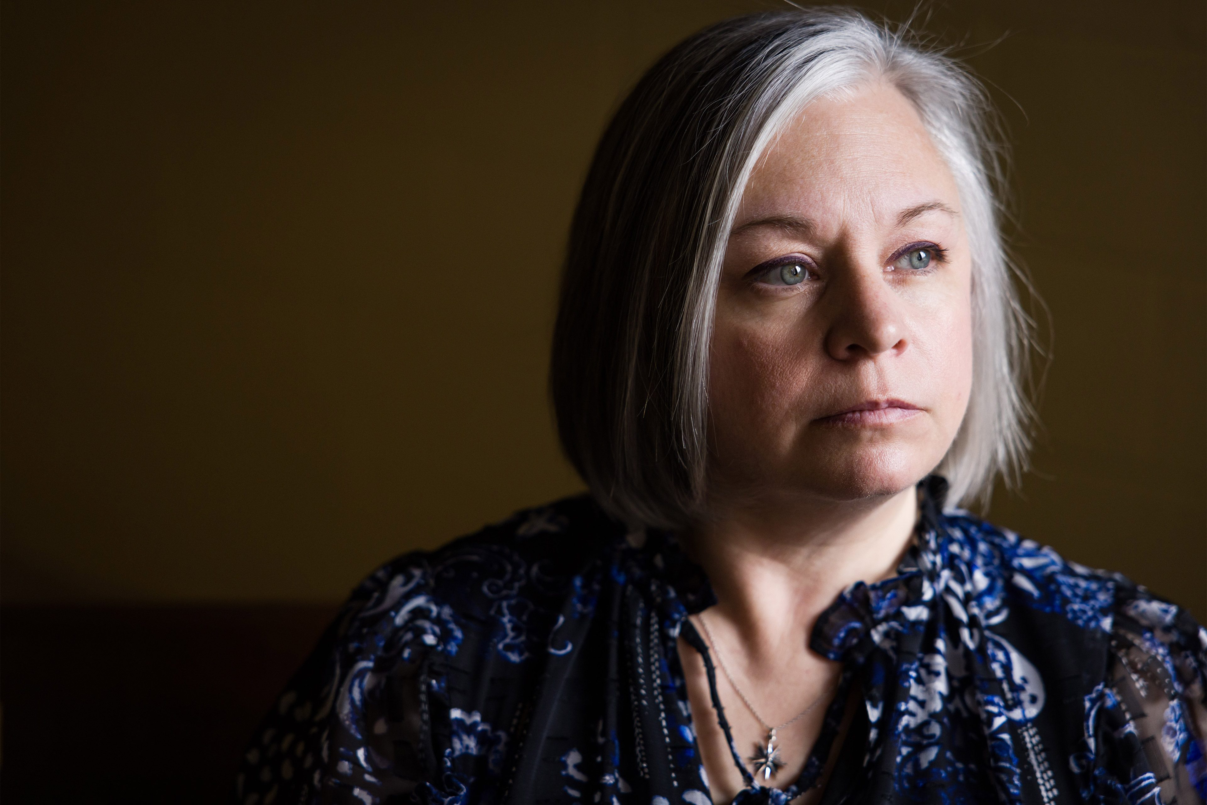 A portrait of a woman standing near a window or light source, casting dramatic shadows on half of her face.