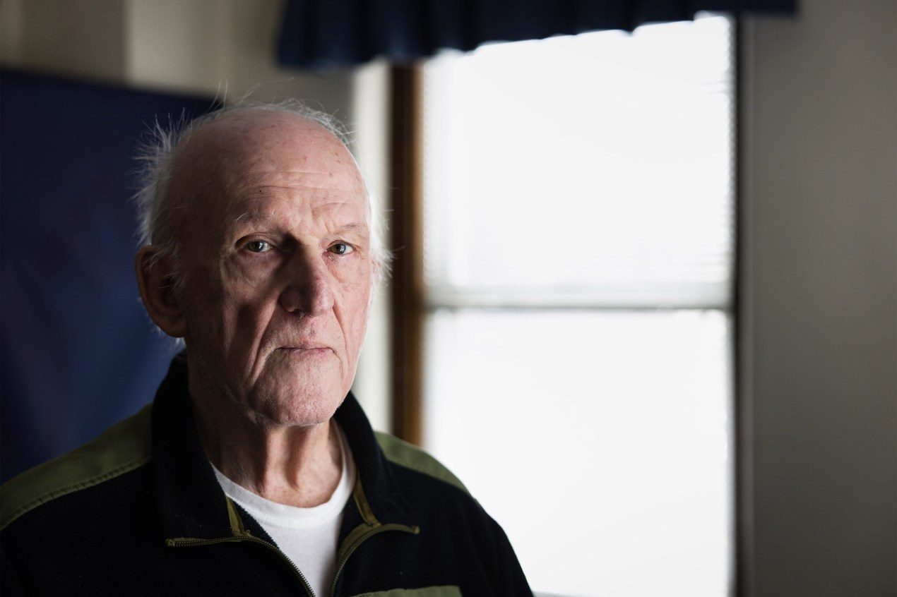 A man stands in front of  a window, casting harsh light on the right side of his face.