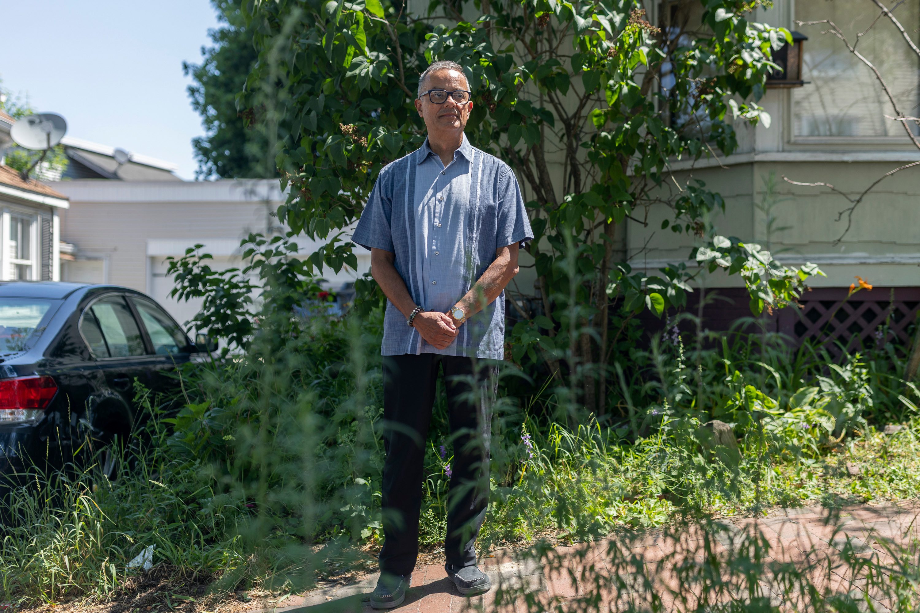 A photo of Ronmel Rangel standing in an area with green shrubbery outside his home.